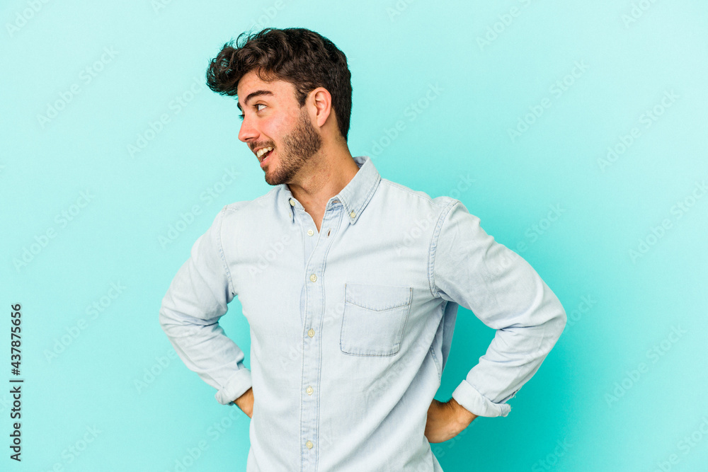 Young caucasian man isolated on blue background laughs happily and has fun keeping hands on stomach. Young caucasian man isolated on blue background laughs happily and has fun keeping hands on stomach.