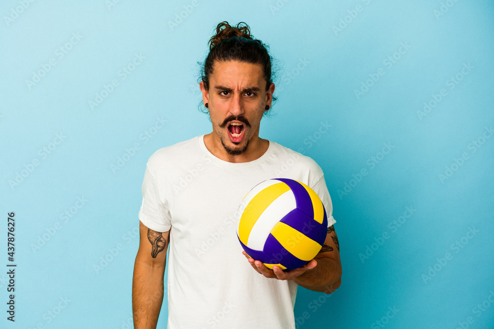 Young caucasian man with long hair isolated on blue background screaming very angry and aggressive.