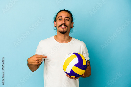 Young caucasian man with long hair isolated on blue background person pointing by hand to a shirt copy space, proud and confident