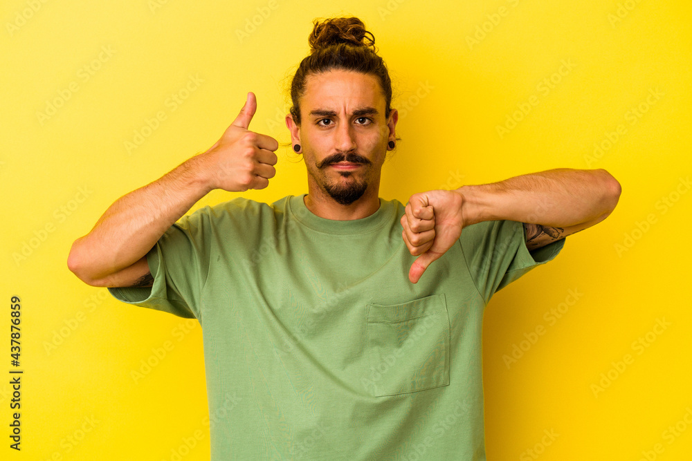 Young caucasian man with long hair isolated on yellow background showing thumbs up and thumbs down, difficult choose concept Young caucasian man with long hair isolated on yellow background showing thumbs up and thumbs down, difficult choose concept