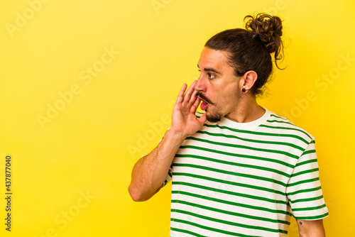 Young caucasian man with long hair isolated on yellow background is saying a secret hot braking news and looking aside © Asier