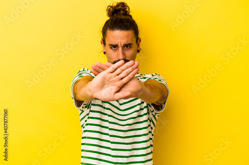 Young caucasian man with long hair isolated on yellow background standing with outstretched hand showing stop sign, preventing you.