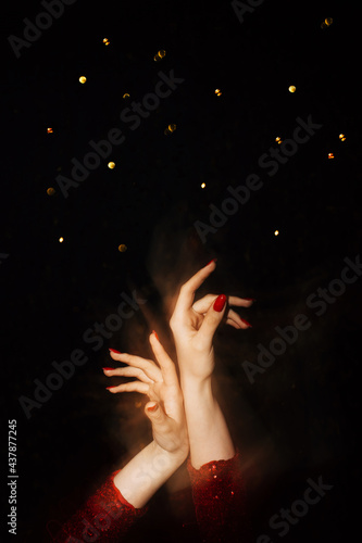 Holiday background. Elegance beauty. Festive joy. Birthday party. Female hands holding together long exposure golden confetti spangles around isolated black copy space.