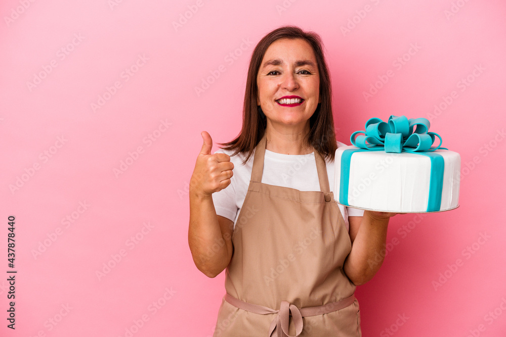 Middle aged pastry chef woman holding a cake isolated on blue background smiling and raising thumb up Middle aged pastry chef woman holding a cake isolated on blue background smiling and raising thumb up