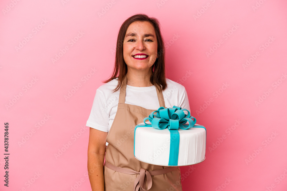 Middle aged pastry chef woman holding a cake isolated on blue background happy, smiling and cheerful. Middle aged pastry chef woman holding a cake isolated on blue background happy, smiling and cheerful.