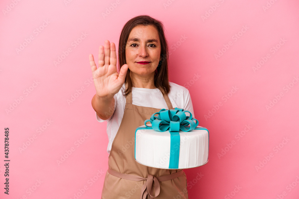 Middle aged pastry chef woman holding a cake isolated on blue background standing with outstretched hand showing stop sign, preventing you. Middle aged pastry chef woman holding a cake isolated on blue background standing with outstretched hand showing stop sign, preventing you.