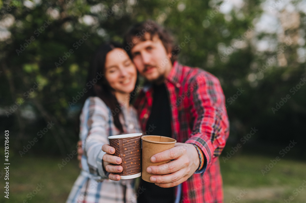 A handsome man and a girl in plaid shirts are resting in nature with hot coffee, tea in an eco-friendly paper cup in their hands. Photography, concept. A handsome man and a girl in plaid shirts are resting in nature with hot coffee, tea in an eco-friendly paper cup in their hands. Photography, concept.