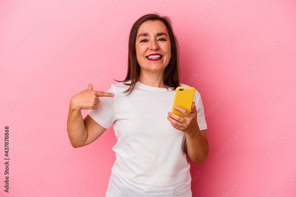 Middle age caucasian woman holding mobile phone isolated on pink background person pointing by hand to a shirt copy space, proud and confident Middle age caucasian woman holding mobile phone isolated on pink background person pointing by hand to a shirt copy space, proud and confident