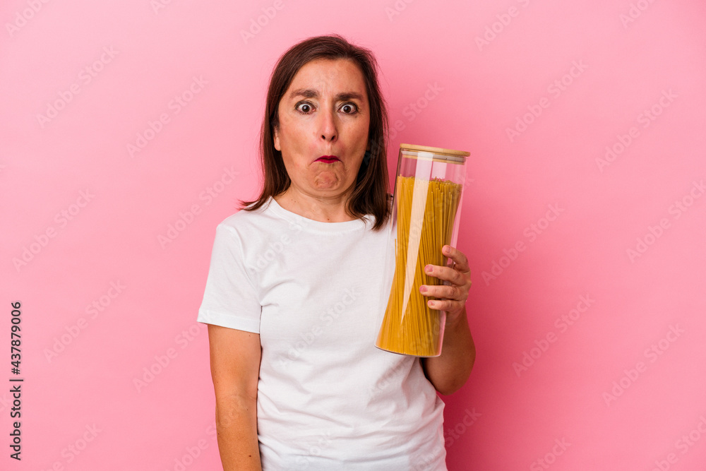 Middle age caucasian woman holding a pasta jar isolated on pink background shrugs shoulders and open eyes confused. Middle age caucasian woman holding a pasta jar isolated on pink background shrugs shoulders and open eyes confused.
