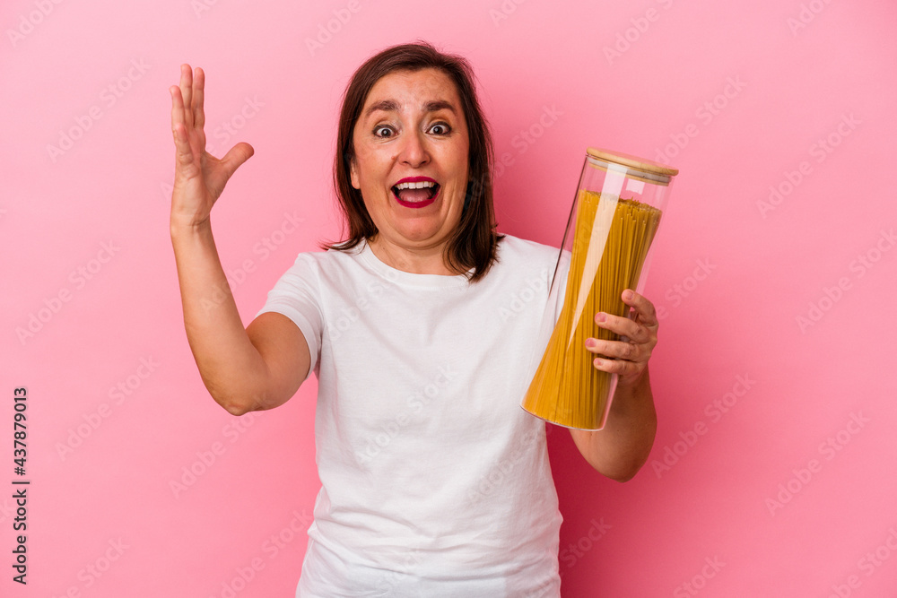 Middle age caucasian woman holding a pasta jar isolated on pink background receiving a pleasant surprise, excited and raising hands. Middle age caucasian woman holding a pasta jar isolated on pink background receiving a pleasant surprise, excited and raising hands.