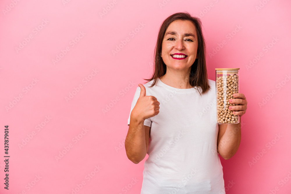 Middle age caucasian man holding a chickpeas jar isolated on pink background smiling and raising thumb up Middle age caucasian man holding a chickpeas jar isolated on pink background smiling and raising thumb up