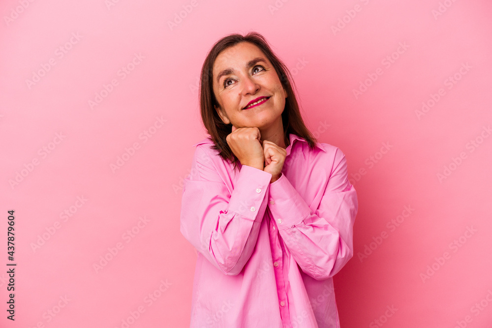 Middle age caucasian woman isolated on pink background keeps hands under chin, is looking happily aside. Middle age caucasian woman isolated on pink background keeps hands under chin, is looking happily aside.