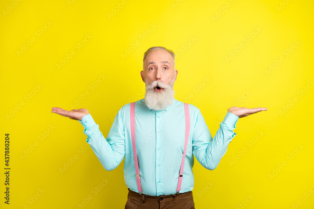 Photo of impressed aged man hold empty space wear blue shirt isolated on vivid yellow color background Photo of impressed aged man hold empty space wear blue shirt isolated on vivid yellow color background
