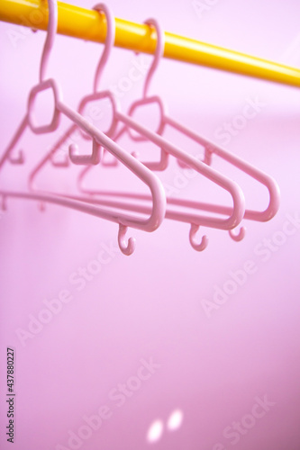 Set of three pink clothes hangers hang on a yellow rack on a pink background