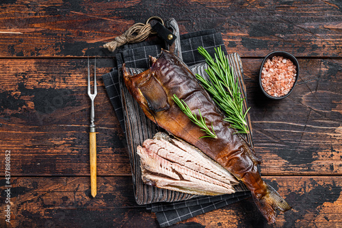 Cut Hot smoked fish on a wooden board with rosemary. Dark wooden background. Top view