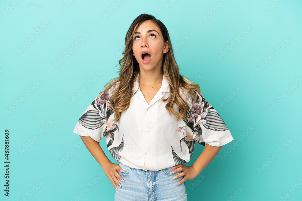 Young woman over isolated blue background looking up and with surprised expression Young woman over isolated blue background looking up and with surprised expression