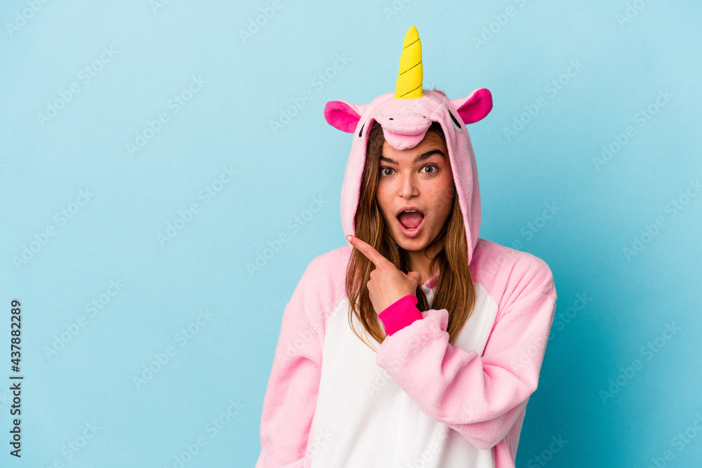Young caucasian woman wearing a unicorn pajama isolated on blue background pointing to the side