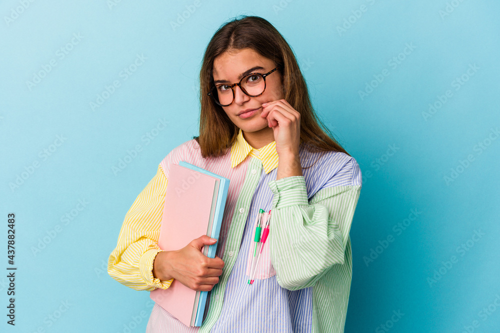 Young caucasian student woman holding books isolated on blue background with fingers on lips keeping a secret. Young caucasian student woman holding books isolated on blue background with fingers on lips keeping a secret.
