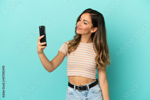 Young woman over isolated blue background making a selfie