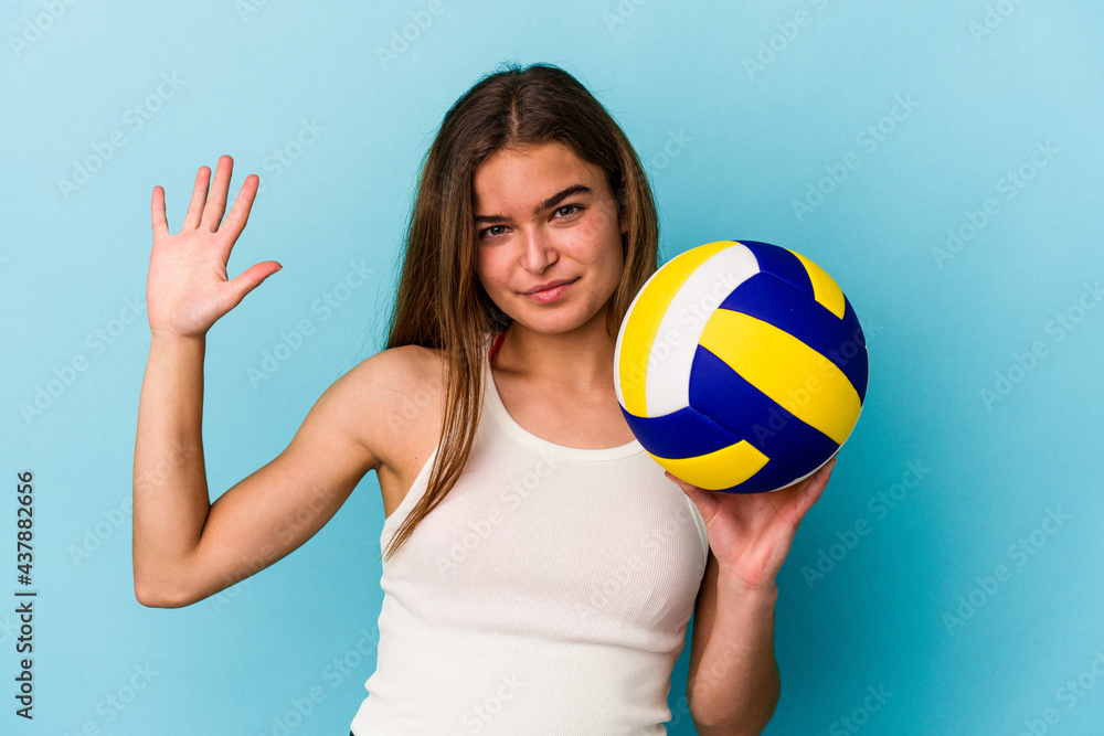 Young caucasian woman playing volleyball isolated on blue background smiling cheerful showing number five with fingers. Young caucasian woman playing volleyball isolated on blue background smiling cheerful showing number five with fingers.