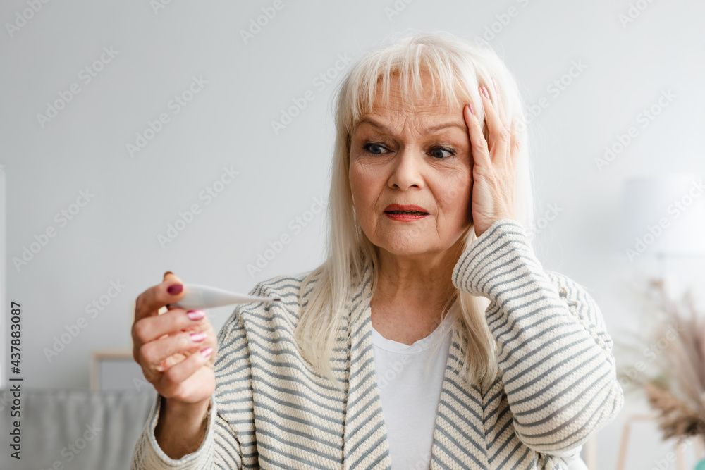Obraz premium Scared mature woman checking body temperature looking at thermometer
