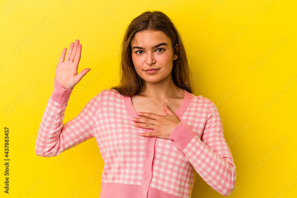 Young caucasian woman isolated on yellow background taking an oath, putting hand on chest.