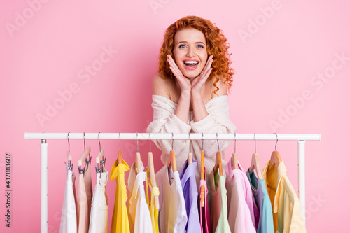 Photo portrait of red haired girl selecting clothes in boutique touching cheeks isolated pastel pink color background