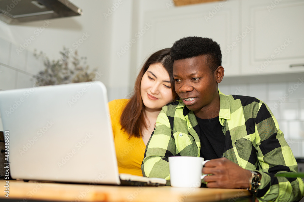 Beautiful African man and asian woman in the kitchen with laptop Beautiful African man and asian woman in the kitchen with laptop