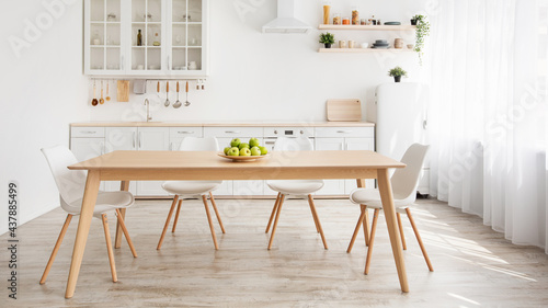 Scandinavian home interior. White and wooden kitchen furniture, plate with apples on dinning table, panorama photo