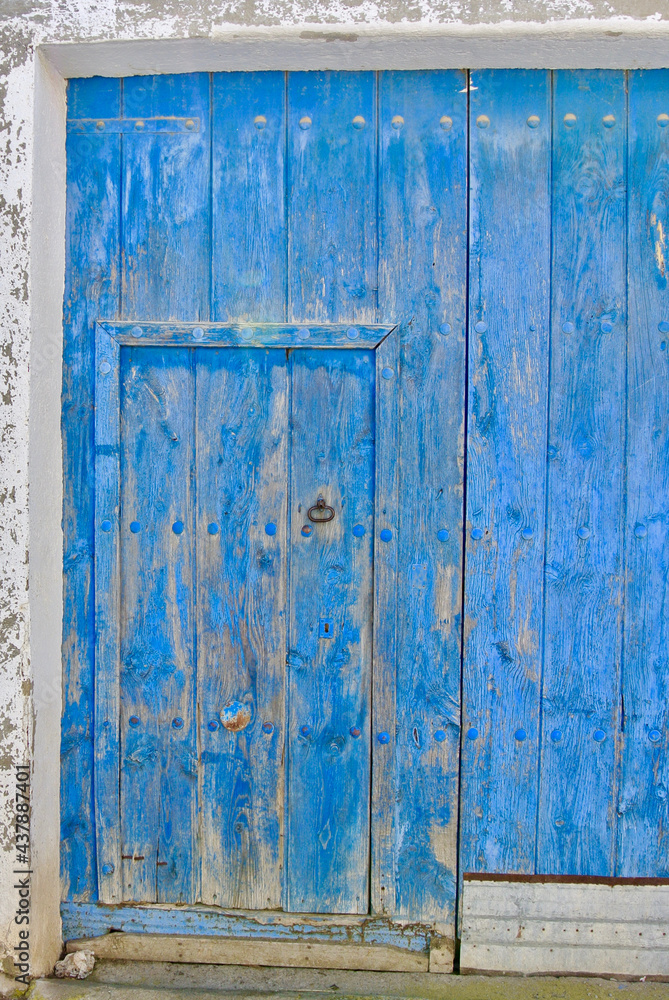 Old blue barn door in the countryside. Closed shabby vintage entrance to the village yard.