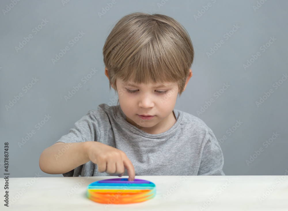 the boy sits at the table and plays a silicone toy antistress popit the boy sits at the table and plays a silicone toy antistress popit