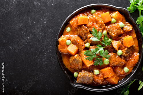 Beef stew with potatoes and carrots in tomato sauce on black background.  Top view, flat lay