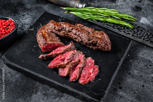 Sliced grilled Onglet Hanging Tender steak on a marble board. Black background. Top view