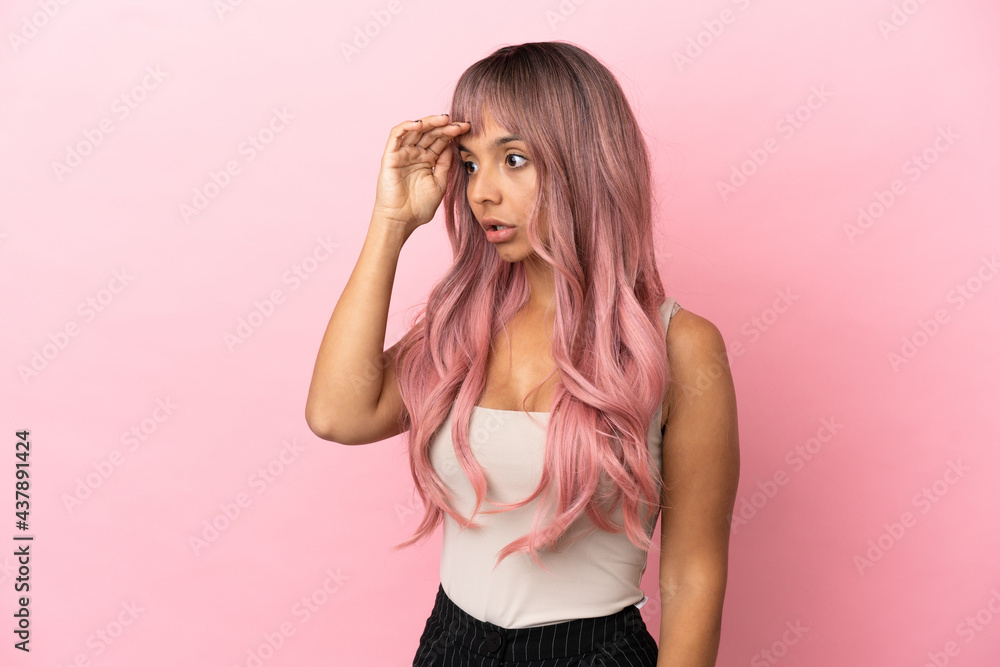 Young mixed race woman with pink hair isolated on pink background with surprise expression while looking side Young mixed race woman with pink hair isolated on pink background with surprise expression while looking side