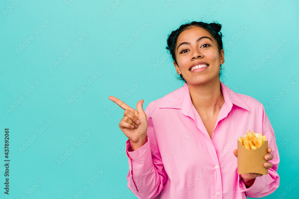 Young latin woman holding chips isolated on blue background smiling and pointing aside, showing something at blank space. Young latin woman holding chips isolated on blue background smiling and pointing aside, showing something at blank space.