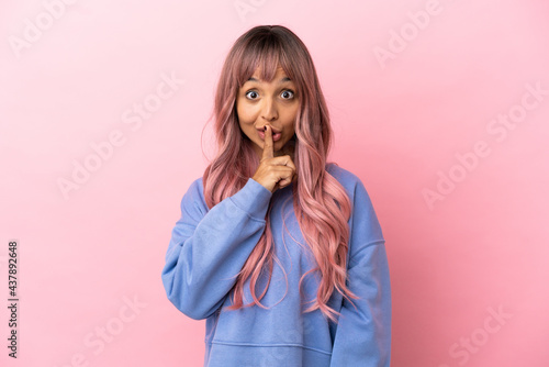 Young mixed race woman with pink hair isolated on pink background showing a sign of silence gesture putting finger in mouth