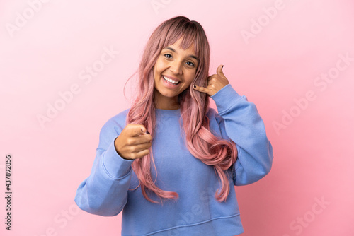 Young mixed race woman with pink hair isolated on pink background making phone gesture and pointing front