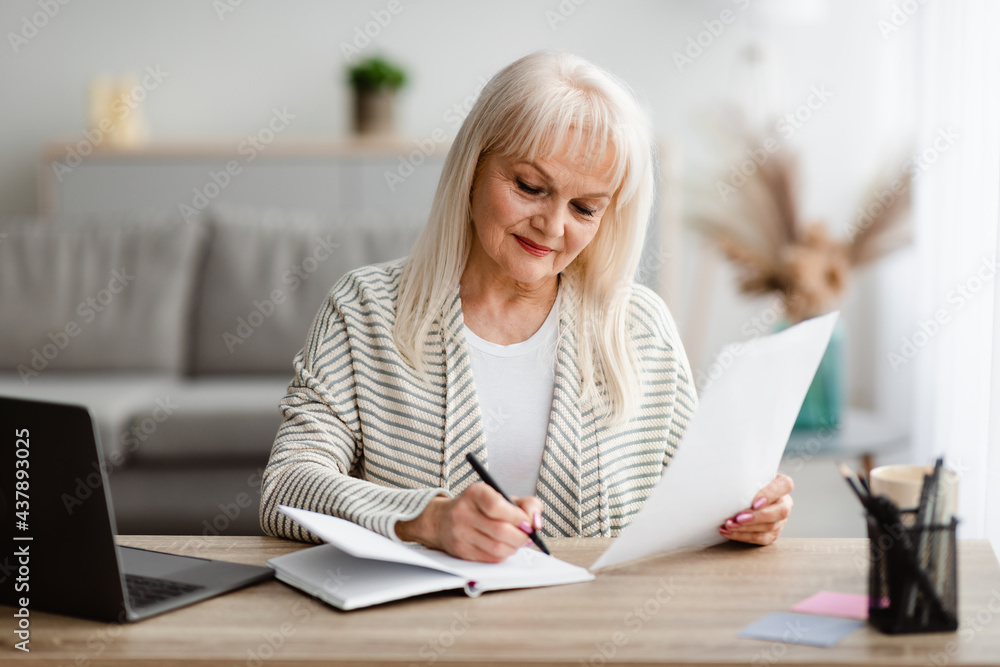 Smiling mature woman writing and holding document at home Smiling mature woman writing and holding document at home