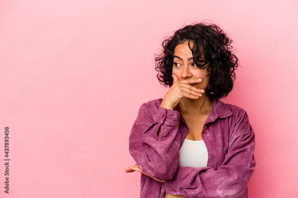 Young curly latin woman isolated on pink background thoughtful looking to a copy space covering mouth with hand. Young curly latin woman isolated on pink background thoughtful looking to a copy space covering mouth with hand.
