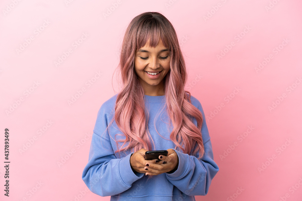 Young mixed race woman with pink hair isolated on pink background sending a message with the mobile Young mixed race woman with pink hair isolated on pink background sending a message with the mobile