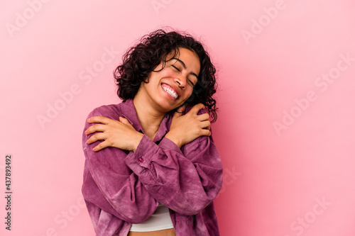 Young curly latin woman isolated on pink background hugs, smiling carefree and happy. © Asier
