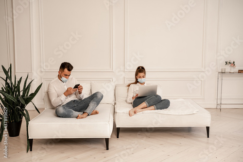 young couple in protective masks using gadgets on sofa in living room © LIGHTFIELD STUDIOS
