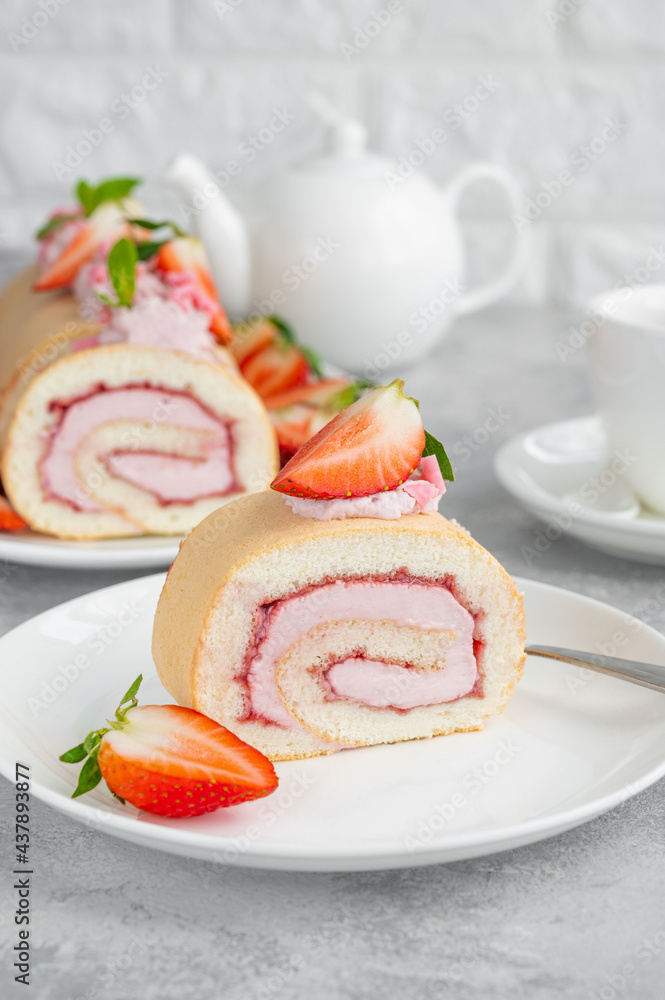 Cake roll with fresh strawberries, jam and cream cheese on a white plate on a gray background. Copy space.
