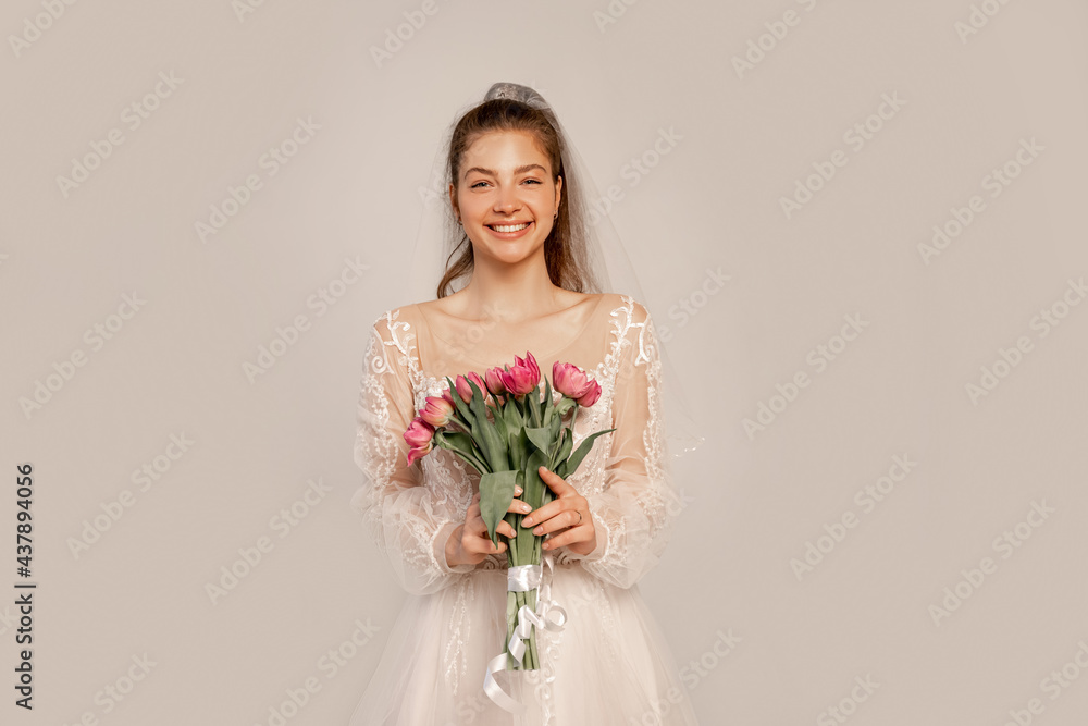 cheerful bride with bouquet of tulips looking at camera isolated on grey cheerful bride with bouquet of tulips looking at camera isolated on grey