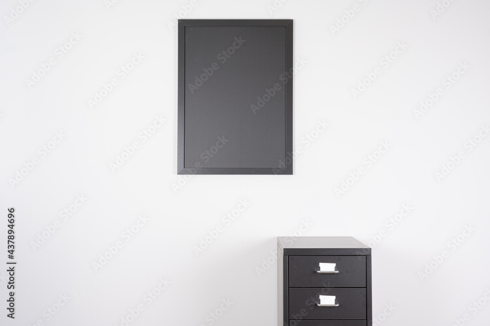 Small blackboard on a white wall and a small, black metal cabinet with drawers and white drawer labels