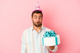 Young caucasian man celebrating his birthday isolated on pink background confused, feels doubtful and unsure.