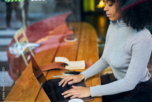 Crop black woman typing on keyboard of laptop while sitting in cafe