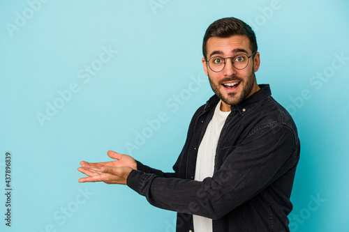 Young caucasian man isolated on blue background holding a copy space on a palm.