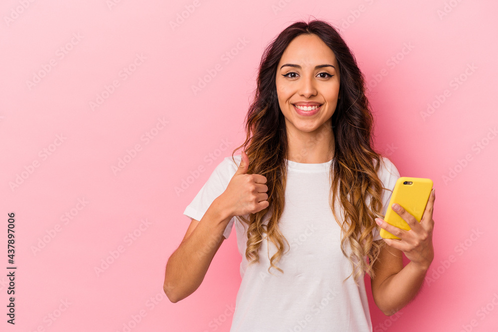 Young mexican woman holding a mobile phone isolated on pink background smiling and raising thumb up Young mexican woman holding a mobile phone isolated on pink background smiling and raising thumb up