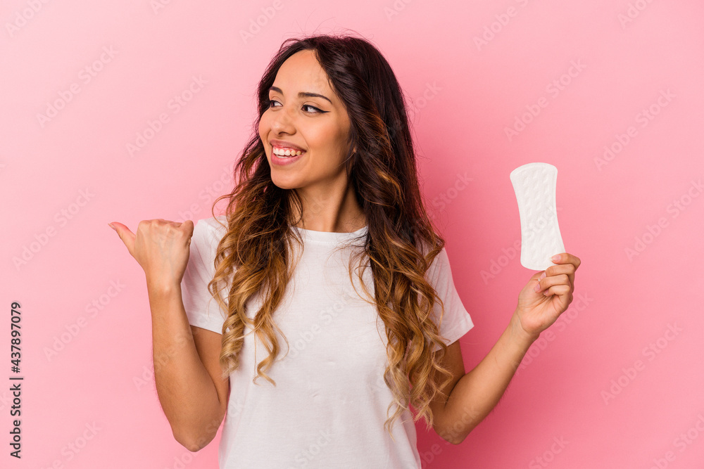Young mexican woman holding a compress isolated on pink background points with thumb finger away, laughing and carefree. Young mexican woman holding a compress isolated on pink background points with thumb finger away, laughing and carefree.
